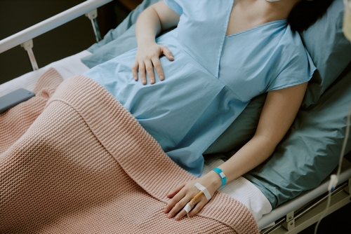 Pregnant woman lying in hospital bed under a blanket