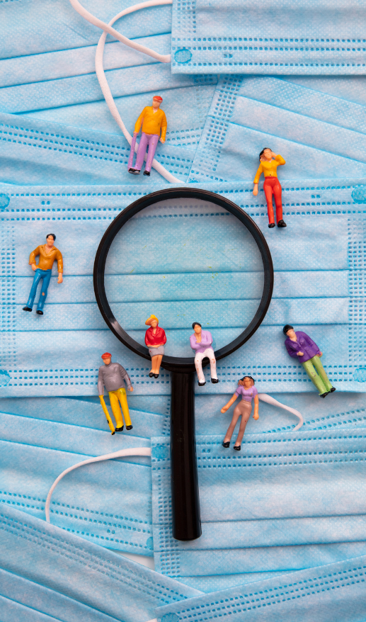 A magnifying glass over disposable face masks with little people figurines around